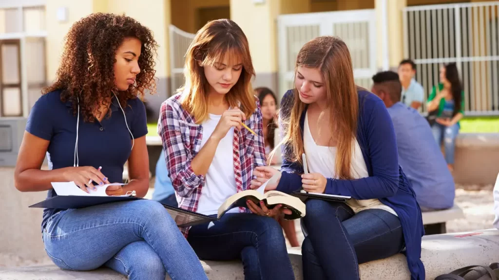 The image shows three girls studying English in the park.